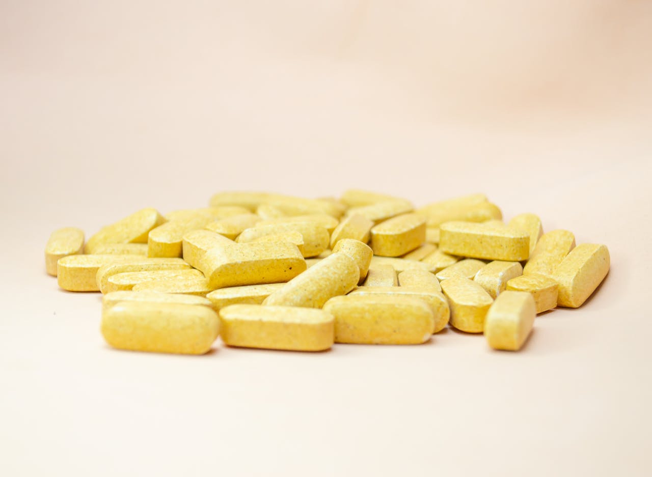 Close-up of scattered yellow vitamin tablets on a light neutral background.