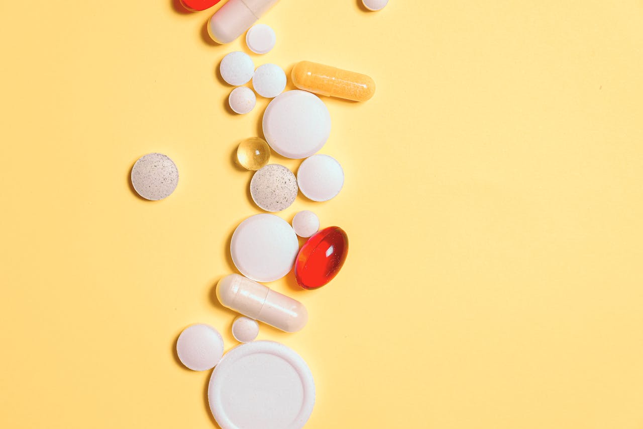 A collection of assorted pills and capsules on a vibrant yellow surface.